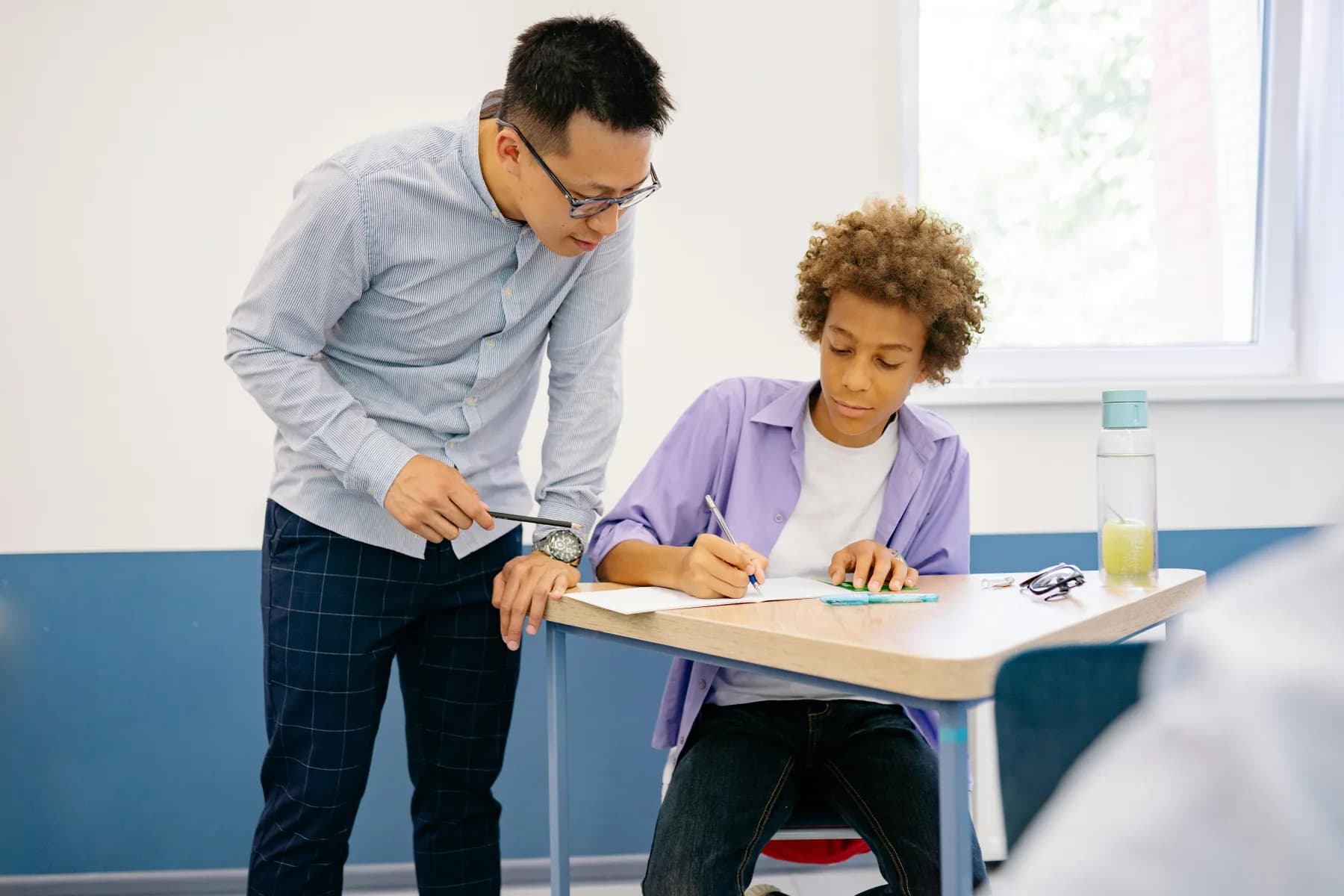 Teacher guiding a secondary-school student through a written exercise